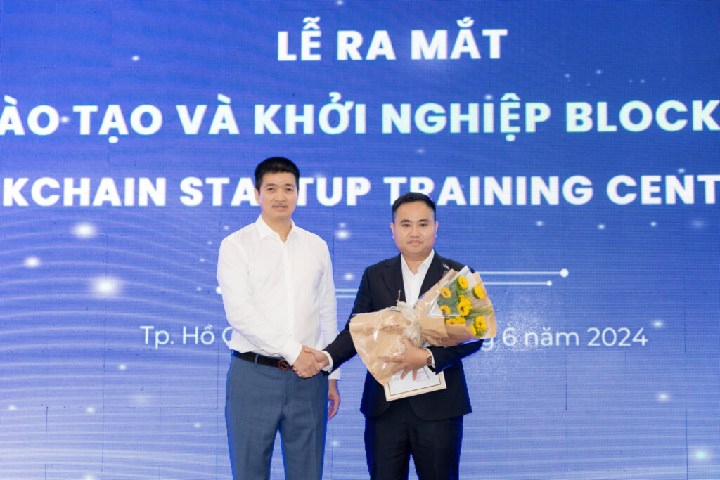 Mr. Phan Duc Trung, the VBA representative, presents flowers and the appointment decision to Mr. Tran Duy Cuong, Director of the Vietnam Blockchain Training and Startup Center