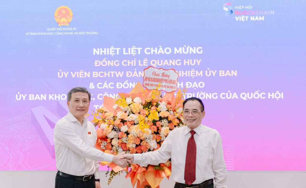 Mr. Hoàng Văn Huây, Chairman of the Vietnam Blockchain Association (right), received congratulatory flowers from Mr. Lê Quang Huy, Member of the Party Central Committee and Chairman of the National Assembly's Committee on Science, Technology, and Environment (left), during the working session.